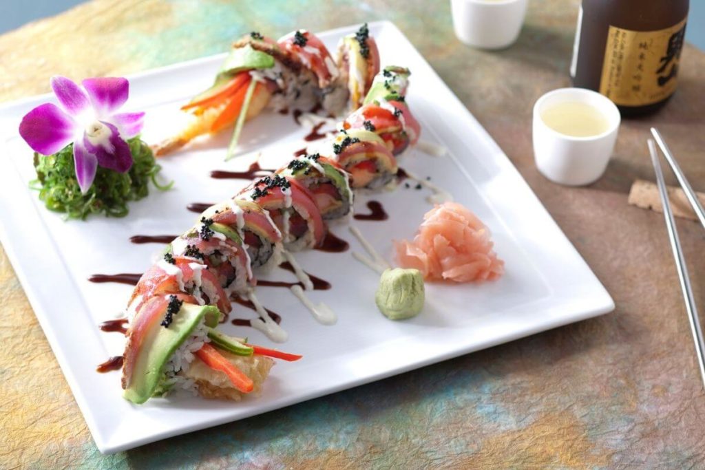 Closeup of a plate with a fancy sushi roll on it, adorned with an orchid.