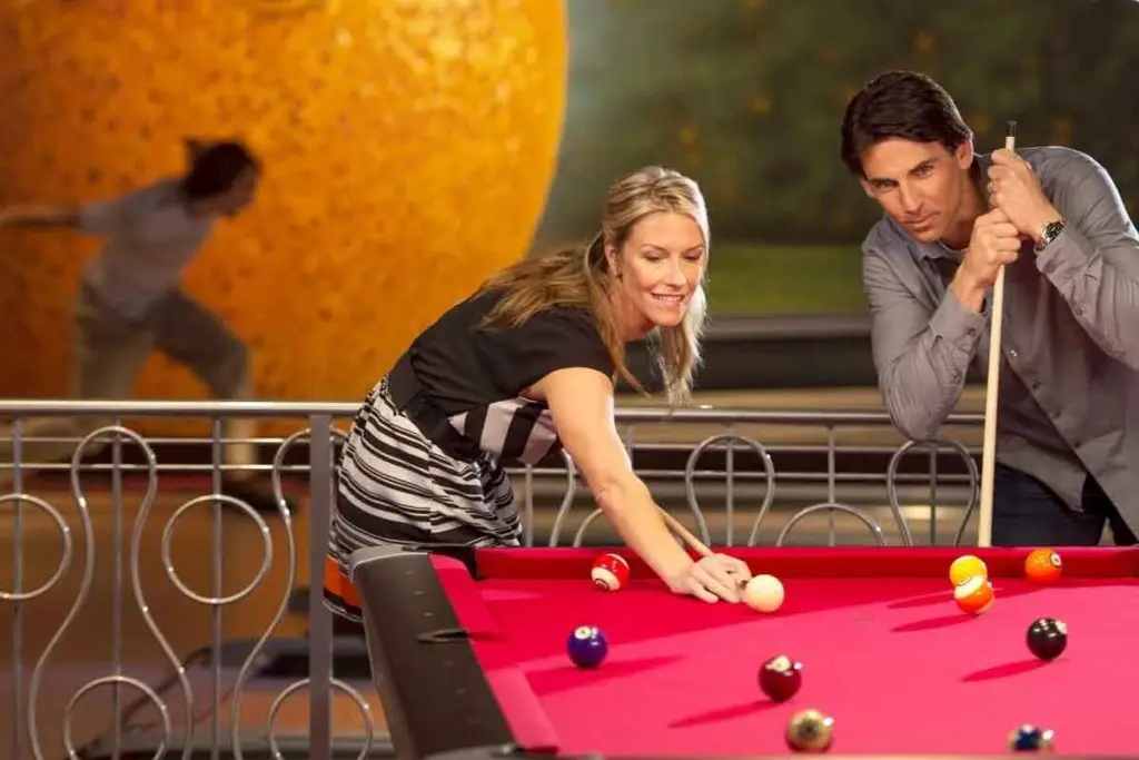 Photo of a man and woman playing pool while a person bowls in the background.