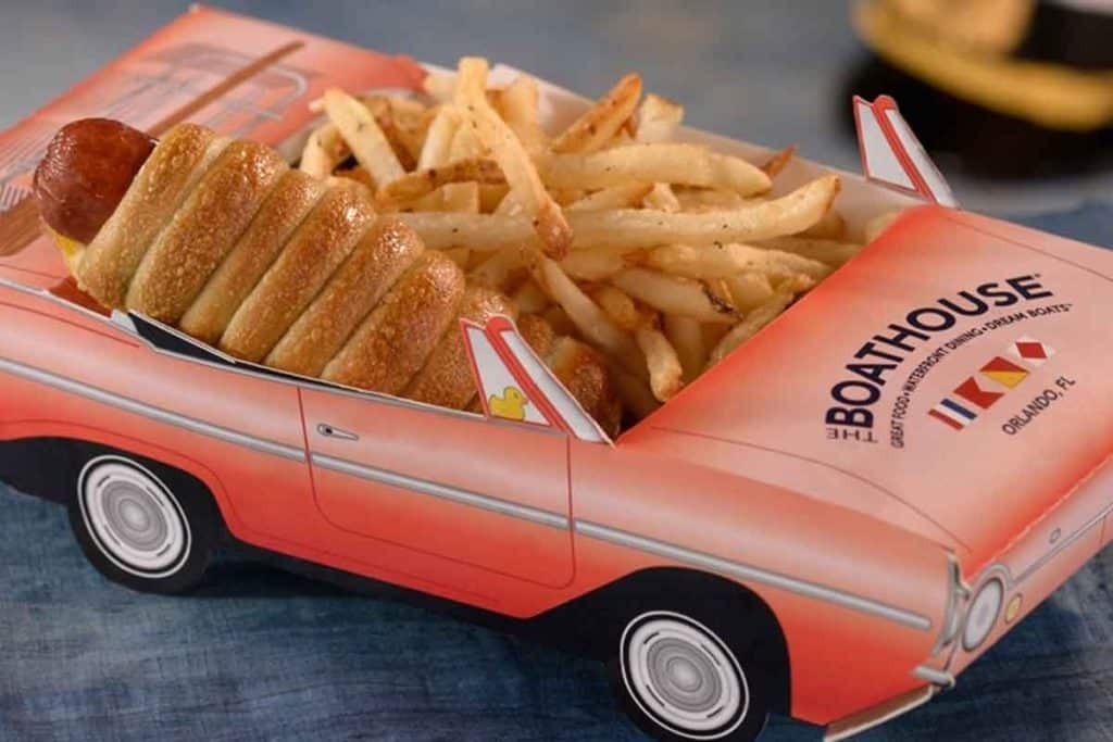 Closeup photo of a hot dog wrapped in a croissant and french fries nestled in a cardboard container shaped like a pink convertible.