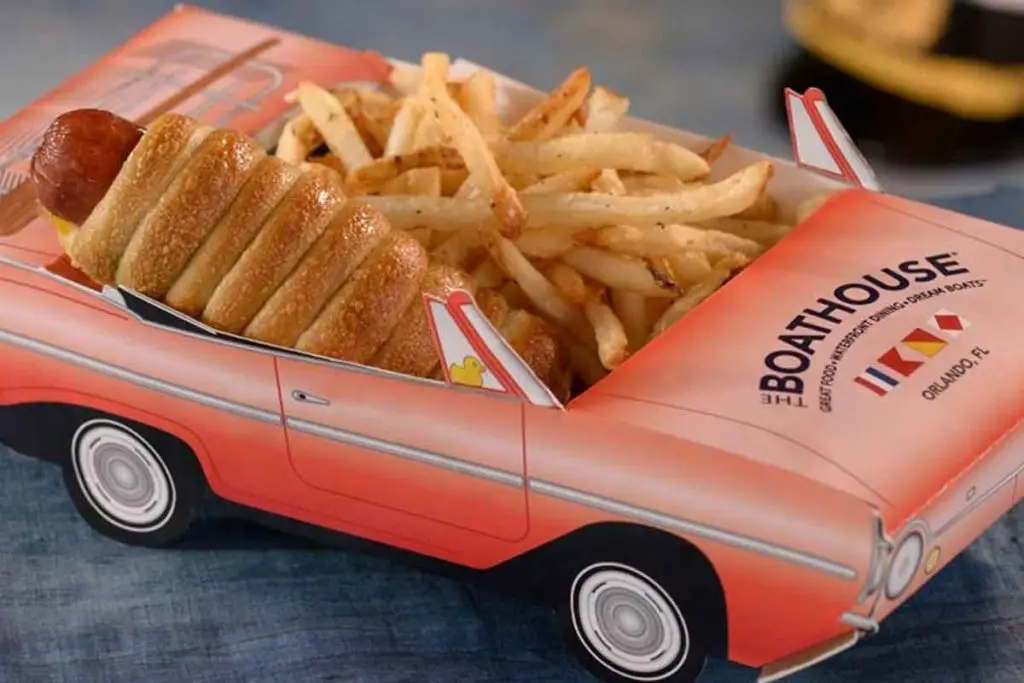 Closeup photo of a hot dog wrapped in a croissant and french fries nestled in a cardboard container shaped like a pink convertible.