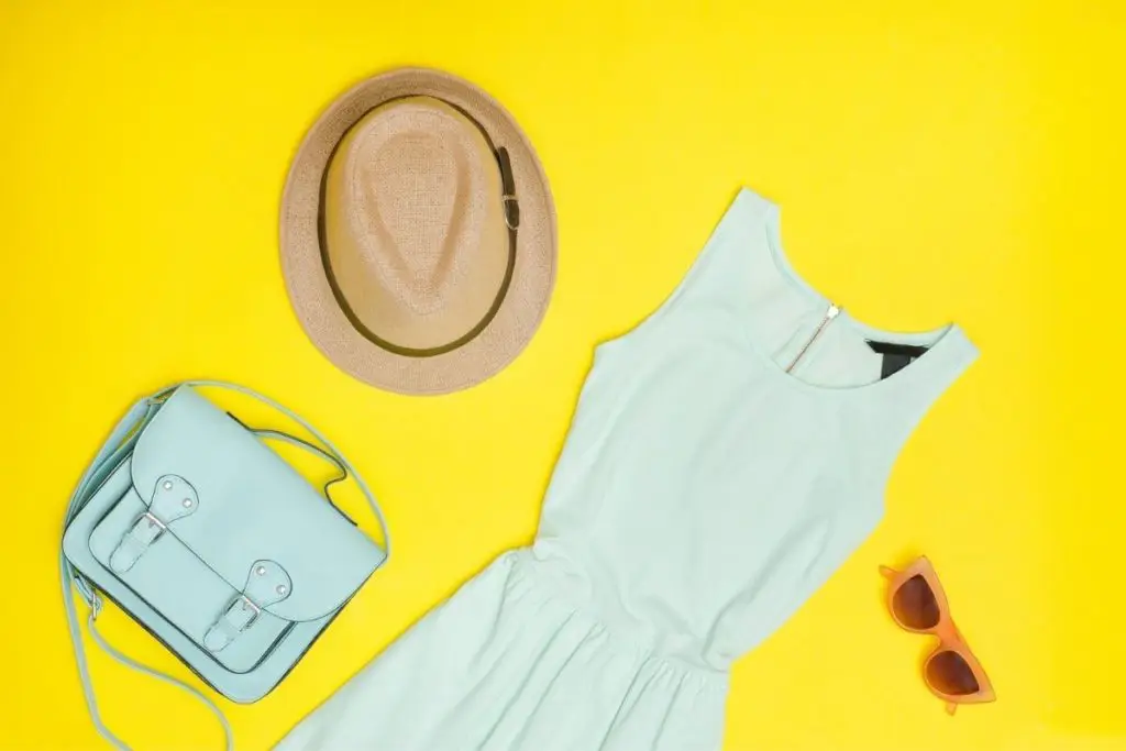 Flat lay photo of a mint handbag, straw hat, coral sunglasses, and a mint jersey tank dress.