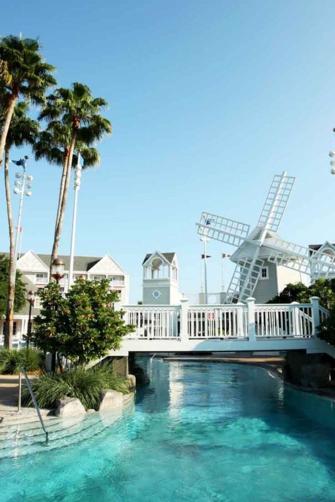 Photograph of a section of the Stormalong Bay pool at Disney World, featuring a white bridge, turquoise water, a windmill, and part of a resort building in the background.
