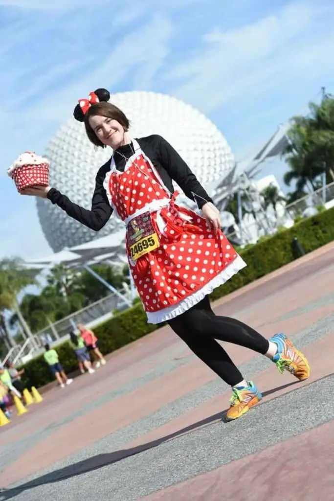 Photo of a woman in running gear with a Minnie Mouse themed apron with the Epcot ball in the background.
