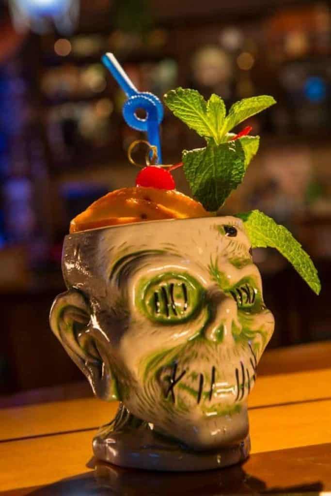 Closeup of a ceramic zombie shaped cup with fruit and a straw poking out the top.