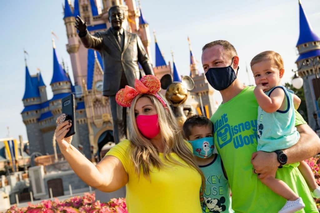 Photo of a man and woman with 2 young boys taking a selfie in front of the Walt Disney and Mickey Mouse statue at Disney World.