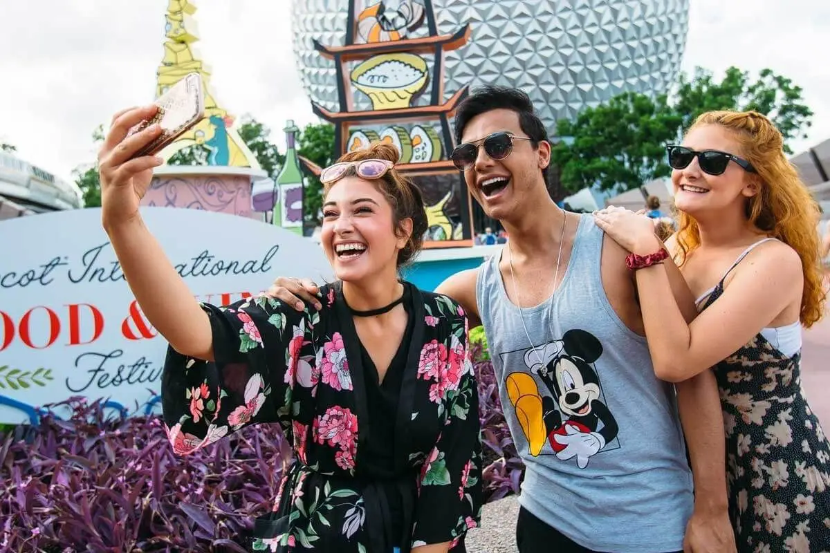 Photo of 3 young adults taking a selfie in front of the Epcot Food and Wine Festival sign.