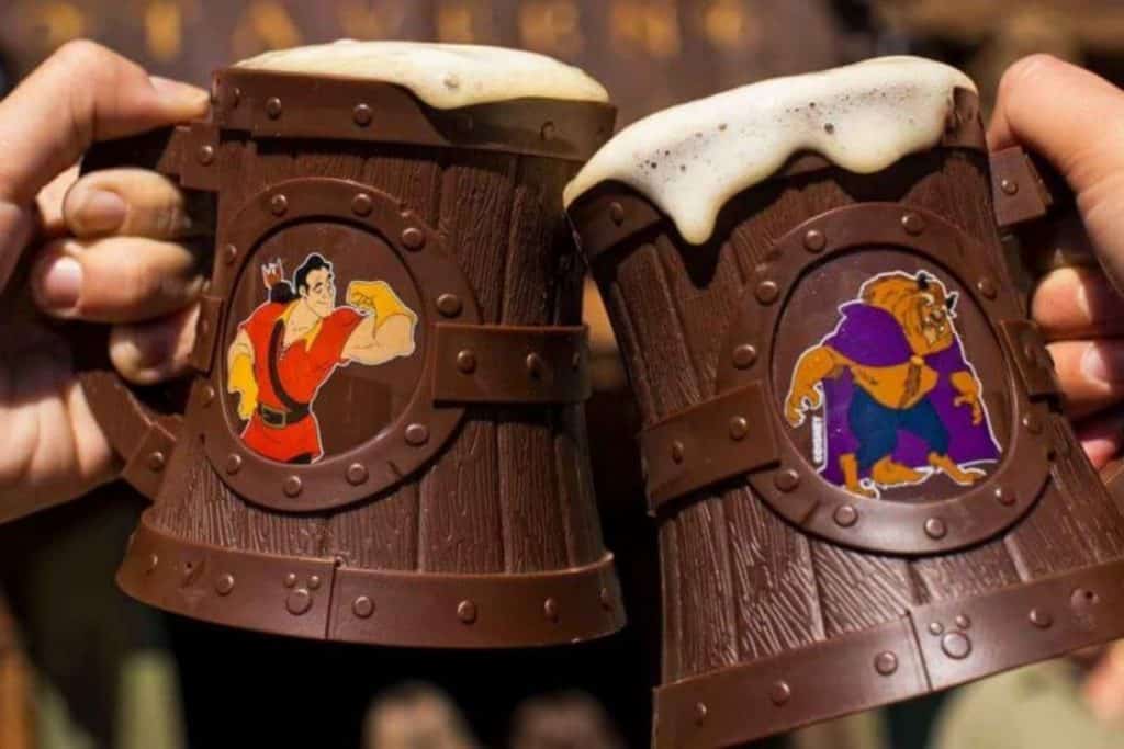 Closeup of 2 people clinking souvenir mugs filled with Lefou's Brew at Disney World's Magic Kingdom.