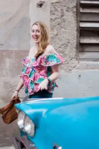 Photo of Meg Frost in Havana, Cuba wearing a brightly colored shirt behind a sky blue retro car.