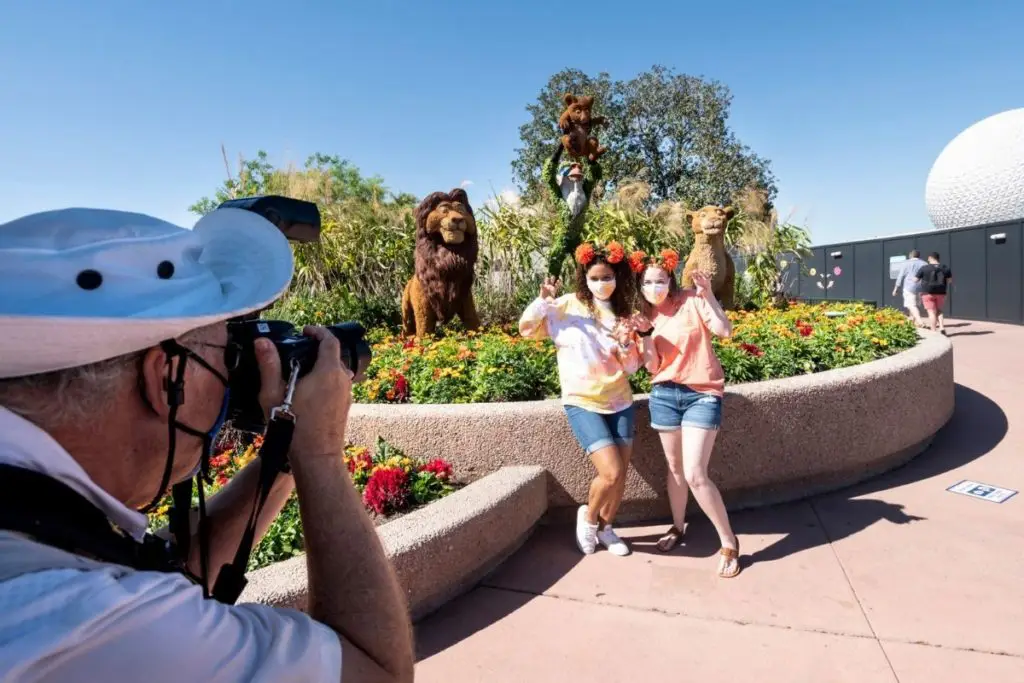 Two young women pose in front of Lion King themed topiaries while a Disney World photographer takes their picture.