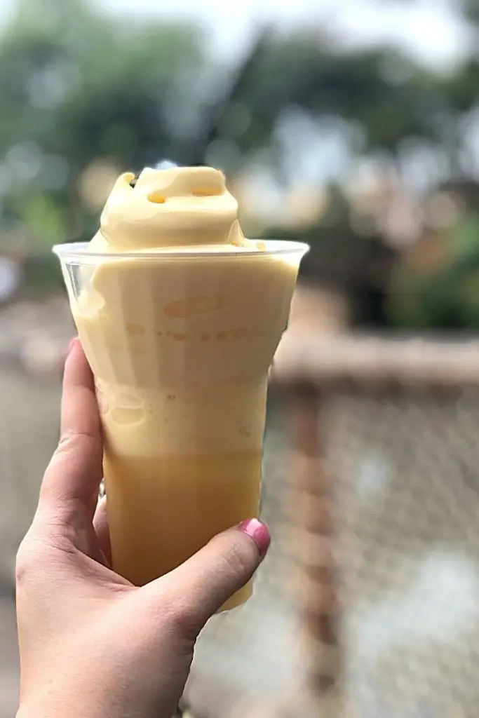 Closeup of a woman holding a cup of pineapple Dole whip soft serve with pineapple juice.
