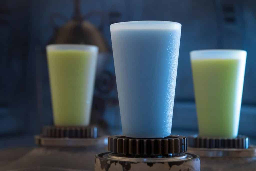 Closeup of 1 glass of blue milk and 2 glasses of green milk.