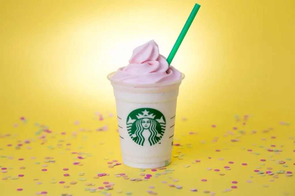 Closeup of a pink strawberry frappucino against a bright yellow background.