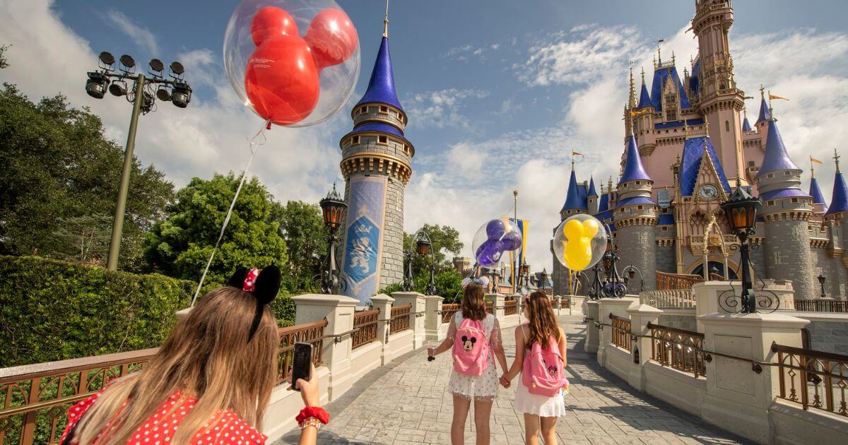 Photo of a woman taking a photo of 2 young girls walking toward Cinderella's Castle at Disney World's Magic Kingdom.