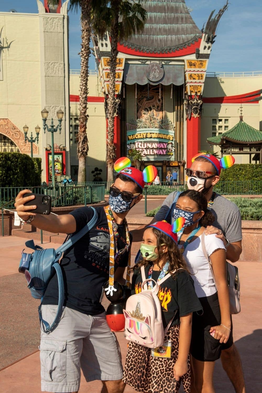 Photo of 2 dads with their 2 daughters taking an Instagram photo in front of Mickey & Minnie's Runaway Railway at Disney World's Hollywood Studios.