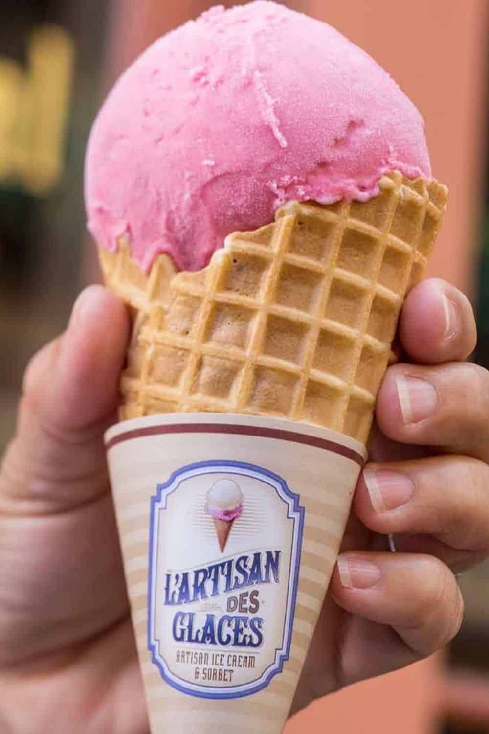 Closeup of a person holding a waffle cone with raspberry gelato from L'Artisan des Glaces at Disney World's Epcot.