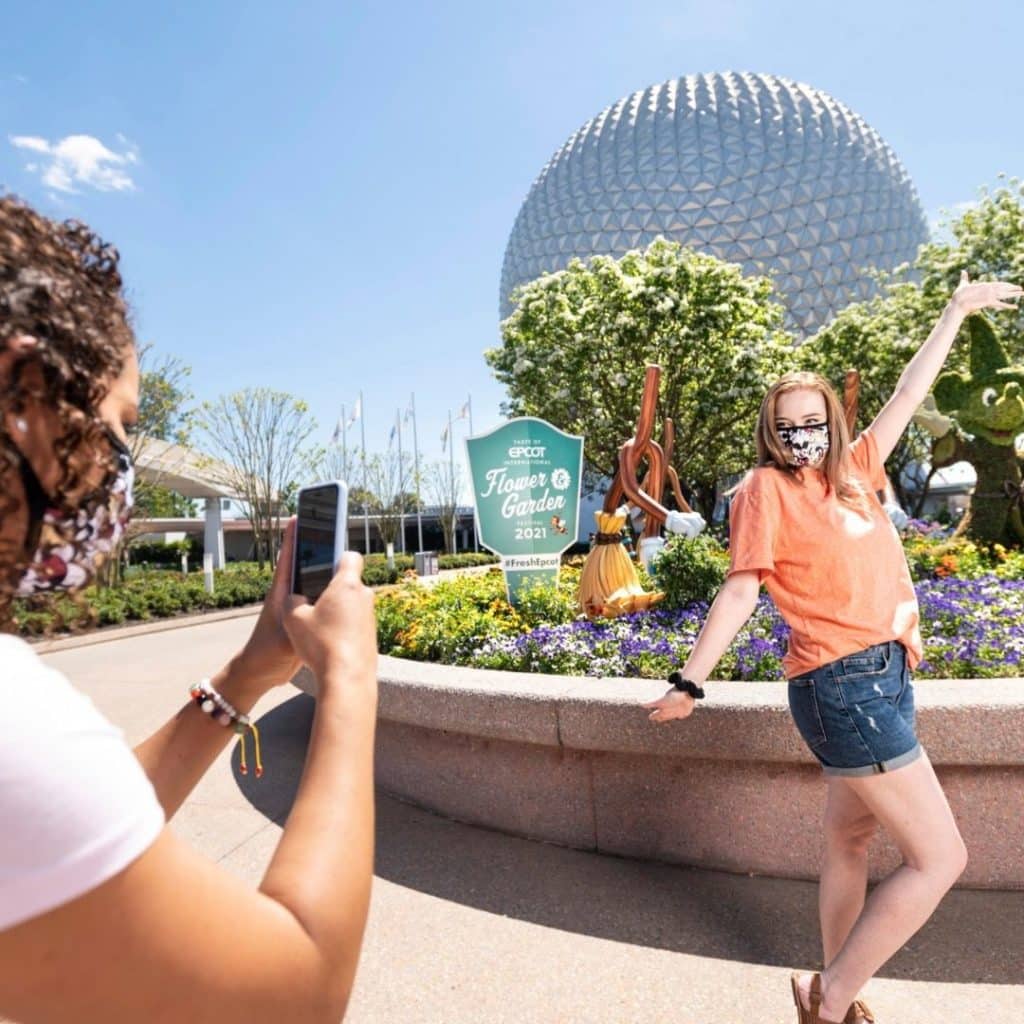 Photo of a woman taking an Instagram photo of her friend posing in front of the iconic Epcot sphere.