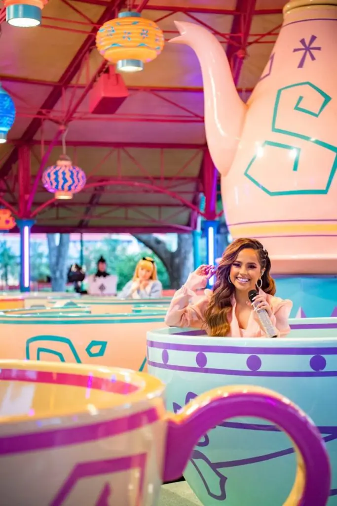 Photo of singer Becky G riding Mad Tea Party ride at Magic Kingdom with Alice in the background.