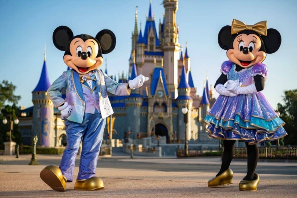 Photo of Mickey and Minnie Mouse in their EARidescent costumes, posing in front of Cinderella's Castle at Disney World's Magic Kingdom.