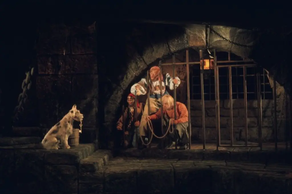 Photo of a scene in Pirates of the Caribbean with 3 pirates in a jail trying to get keys from a dog holding them in his mouth.