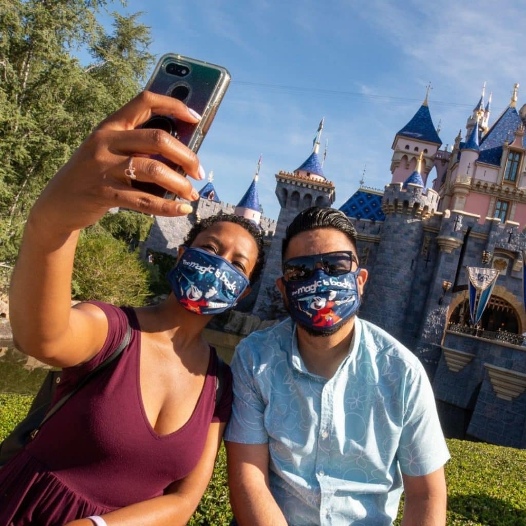 Photo of a couple taking an Instagram photo in front of Sleeping Beauty's castle at Disneyland in California.