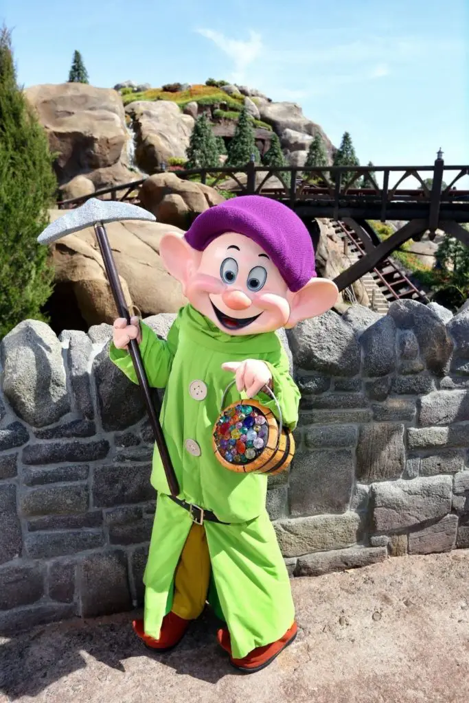 Photo of Dopey holding a hoe and bucket full of jewels outside the Seven Dwarfs Mine Train roller coaster at Magic Kingdom.