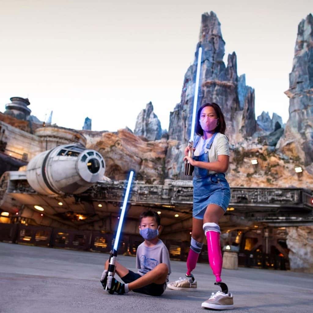 A woman and a young boy pose with lightsabers in front of Star Wars: Galaxy's Edge at Disneyland's California Adventure theme park.