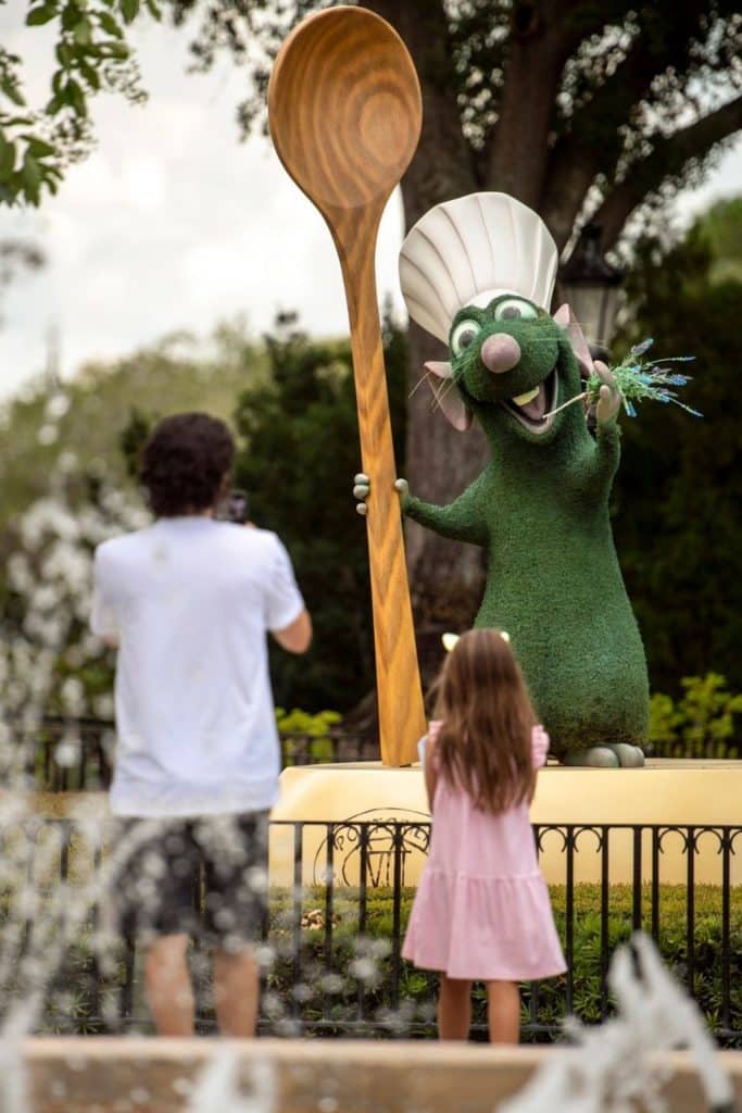 Photo of a boy and a girl from behind while they are looking at a topiary of Remy the chef rat from Ratatouille.
