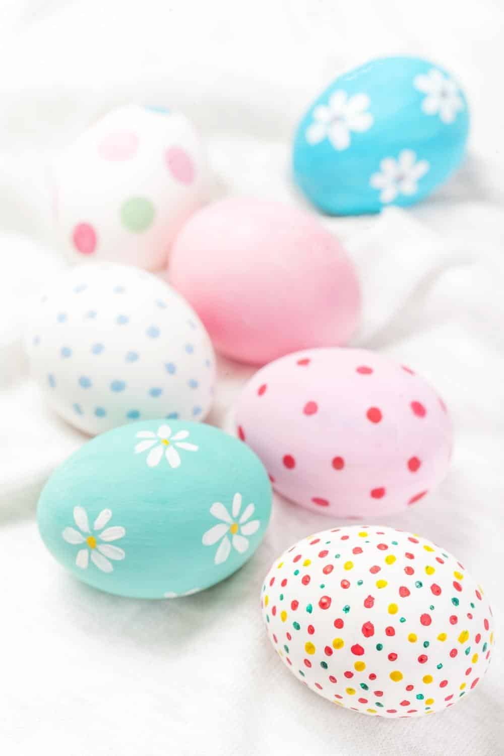 Closeup of 7 pastel decorated Easter eggs on a white surface.