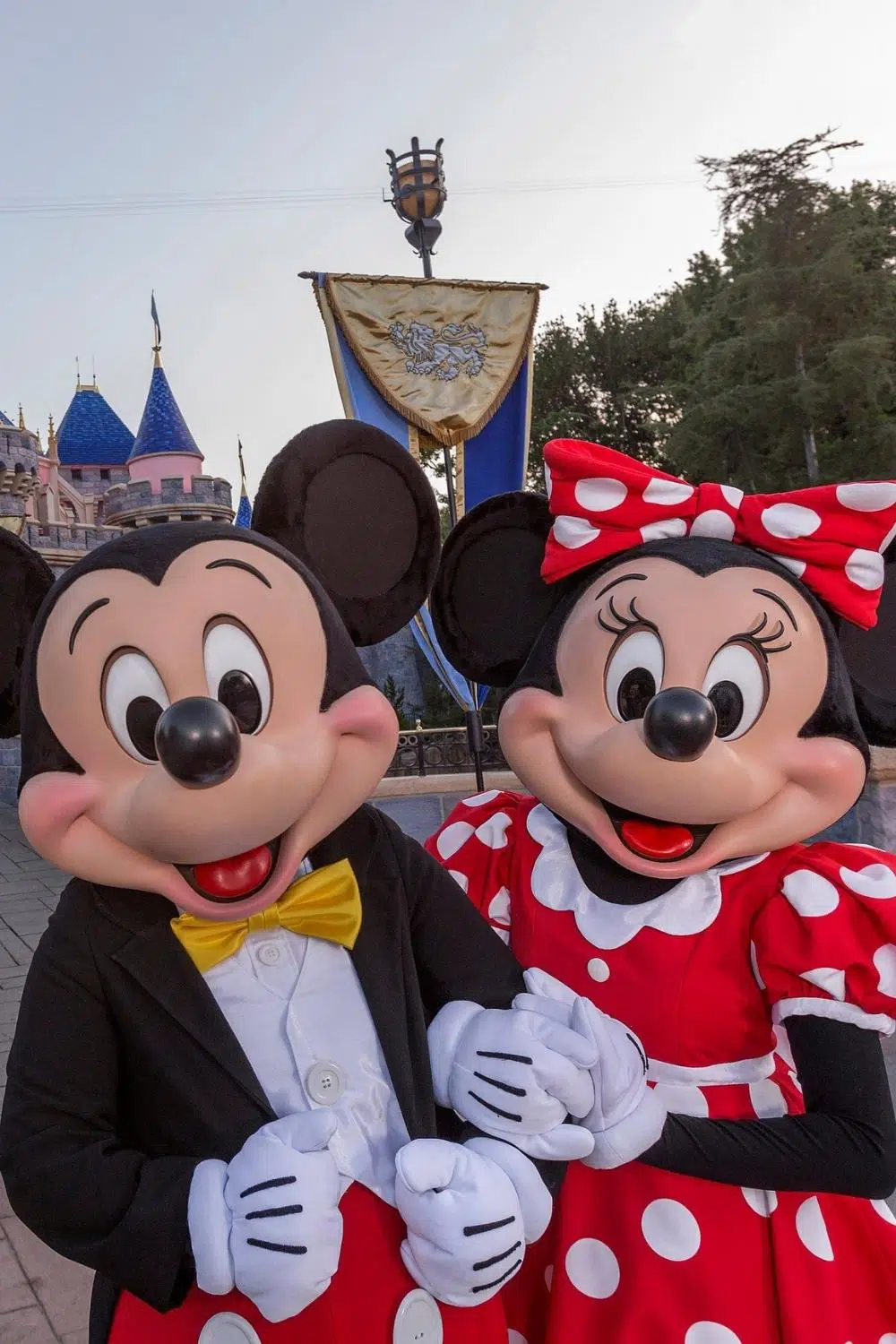 Closeup photo of Mickey and Minnie linking arms in front of Sleeping Beauty's castle at Disneyland.