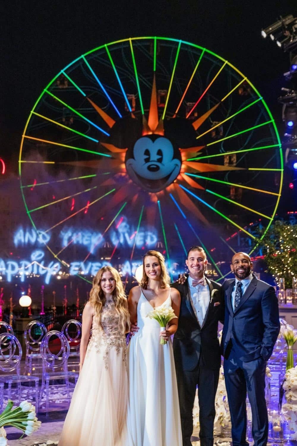 Photo of a bride and groom with Alison Holker Boss and Stephen Twitch Boss posing in front of Mickey's Fun Wheel at Disneyland.