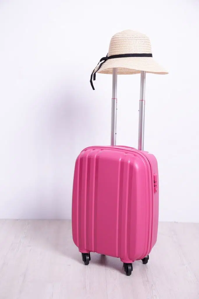 Photo of a pink carry on suitcase with a hat on the handle.