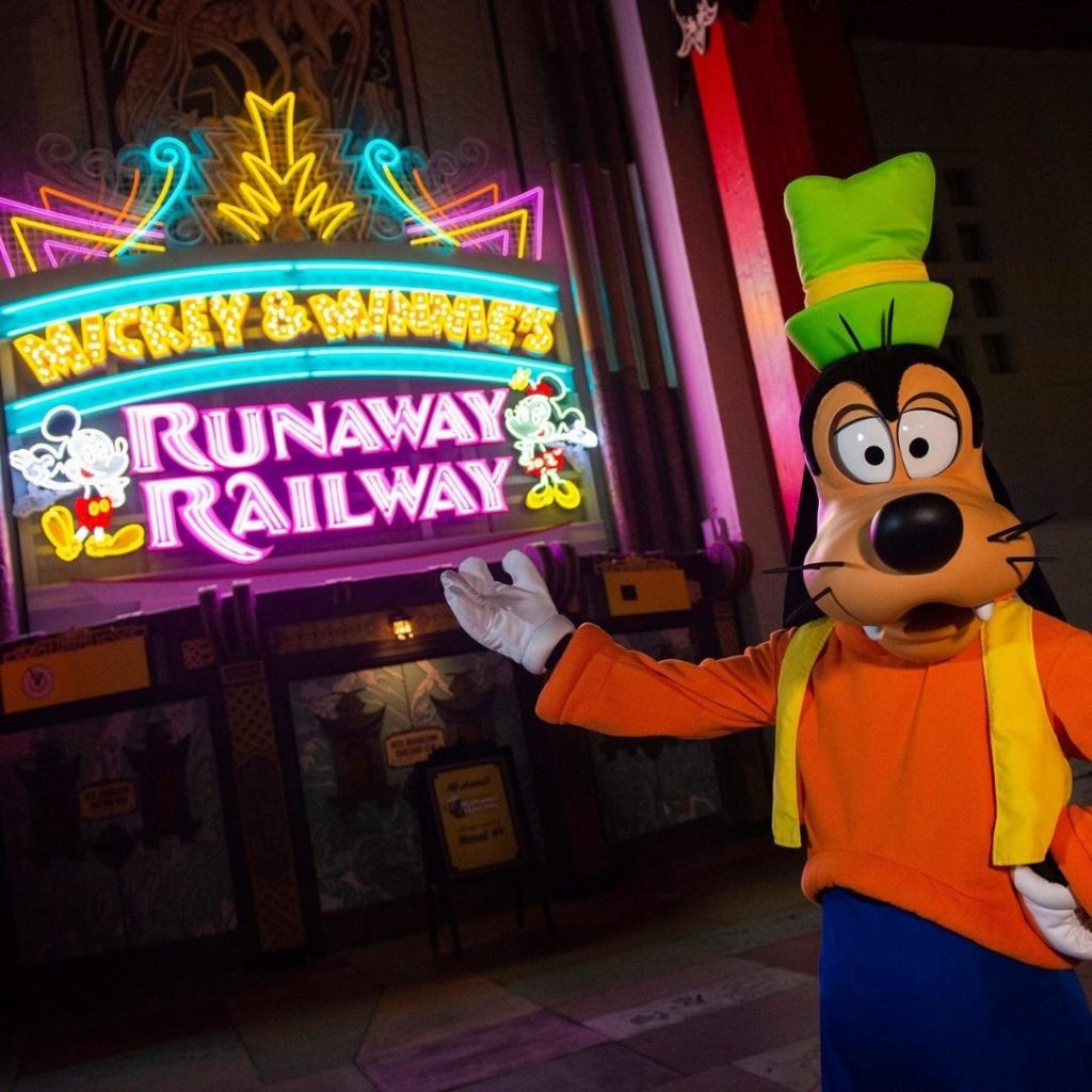 Photo of Goofy pointing to the neon signage for Mickey & Minnie's Runaway Railway at Hollywood Studios.