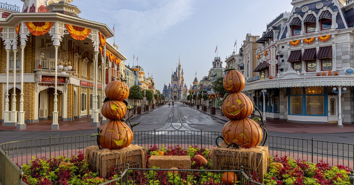 Horizontal photo looking down Main Street toward Cinderella's Castle at Magic Kingdom with a Halloween display in the foreground with hay bales and pumpkins.