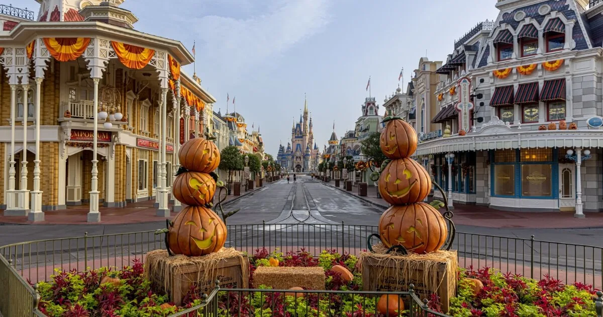 Horizontal photo looking down Main Street toward Cinderella's Castle at Magic Kingdom with a Halloween display in the foreground with hay bales and pumpkins.