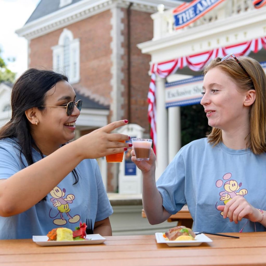 Photo of 2 women clinking glasses while enjoying food at Epcot.