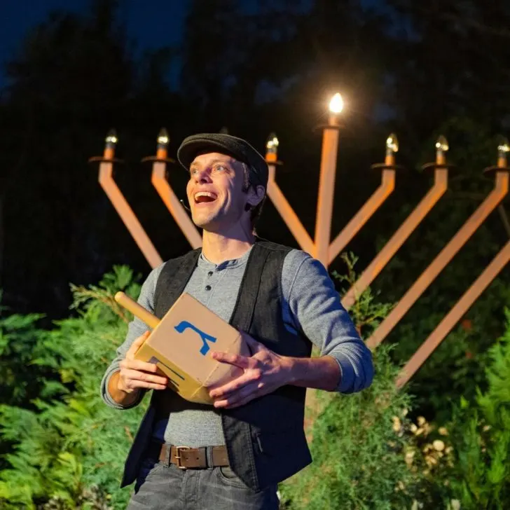 Closeup of a man holding a large dreidel telling the story of Hannukah in front of a large Menorah.