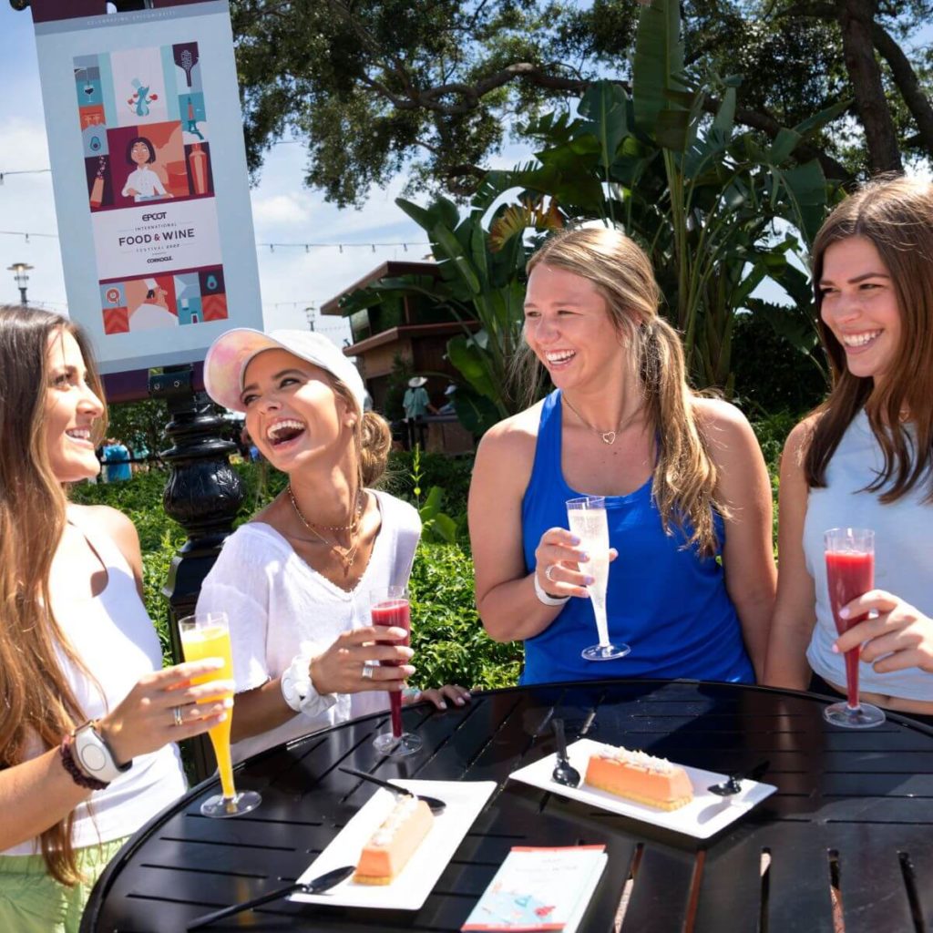 Photo of a group of women wearing tank tops and other light layers while drinking cool beverages at Disney World's Epcot theme park.