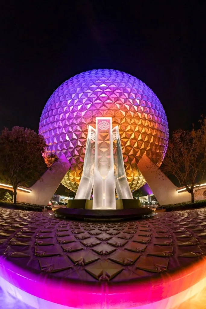 Photo of Spaceship Earth lit up at night with violet, fuchsia, and golden hues.