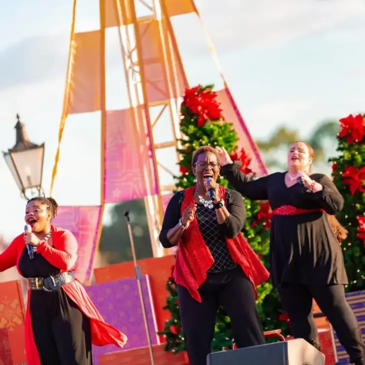 Photo of 3 women performing on a stage with Christmas decorations.