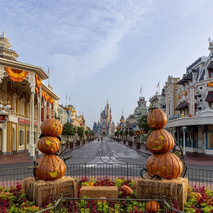 Vertical photo looking down Main Street toward Cinderella's Castle at Magic Kingdom with a Halloween display in the foreground with hay bales and pumpkins.