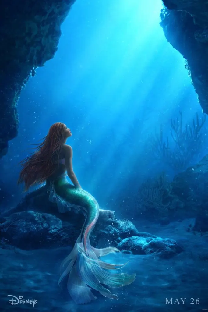 Promotional poster for the live-action version of Disney's The Little Mermaid with a photo of Halley Bailey as Ariel, sitting on a rock under the sea with sunbeams streaming through the water.