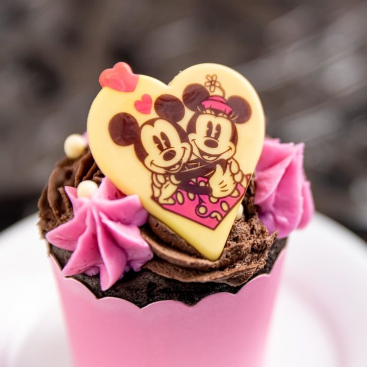 Closeup of a chocolate cupcake with chocolate frosting and Valentine's Day embellishments.