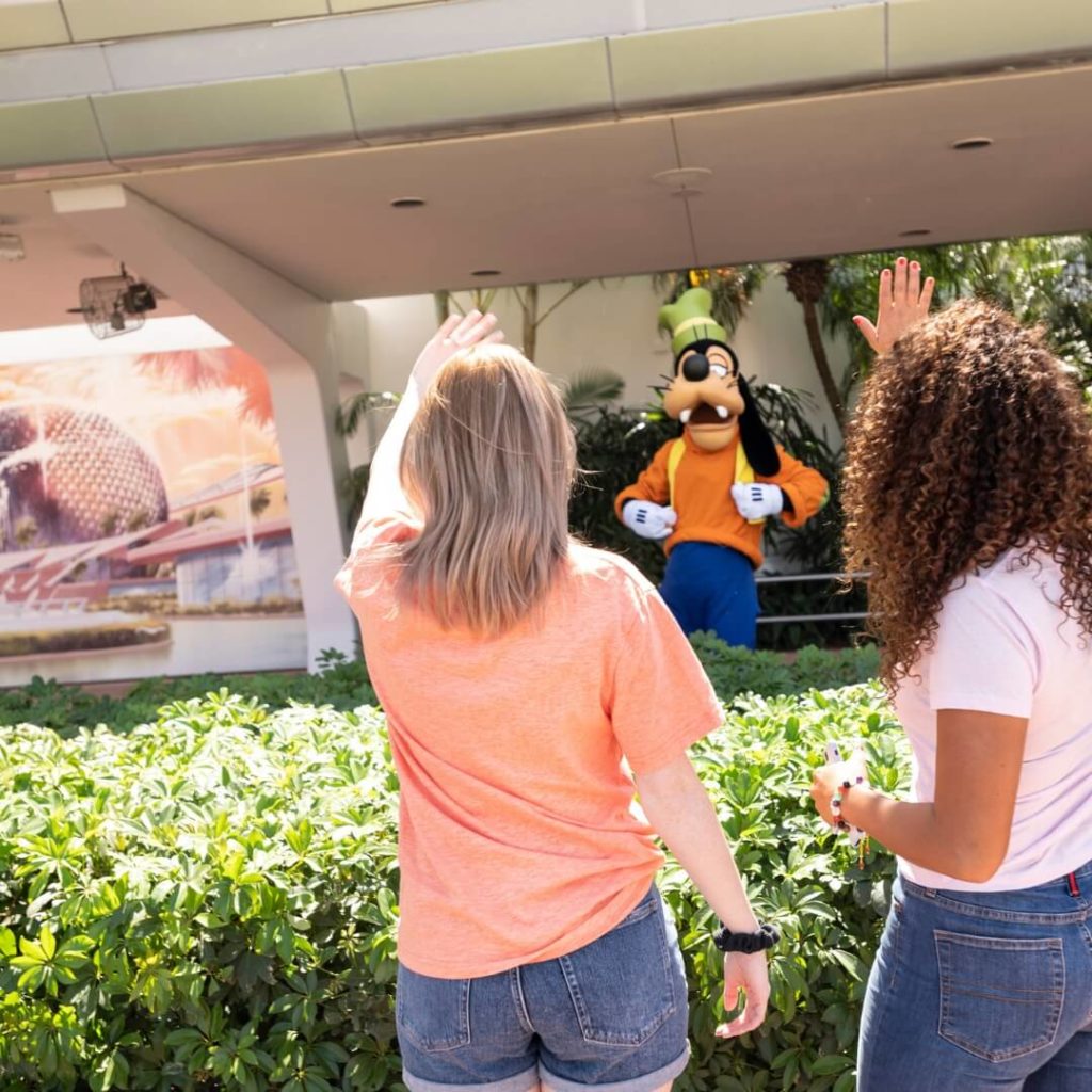 Photo of 2 women with their back to the camera waving at Goofy at Epcot.