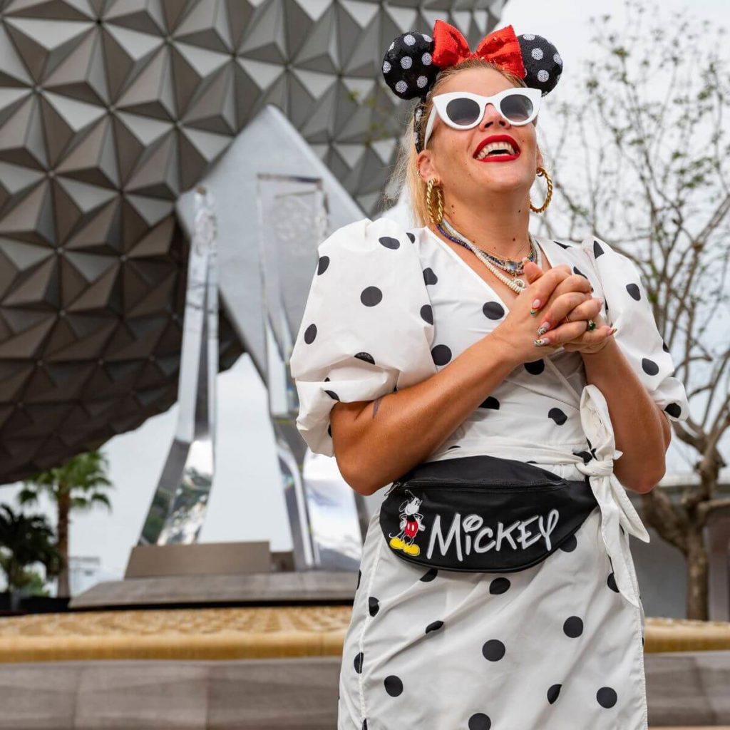 Photo of actress Busy Phillips at Disney World's Epcot wearing sunglasses, and a Minnie Mouse inspired outfit, including Minnie ears.
