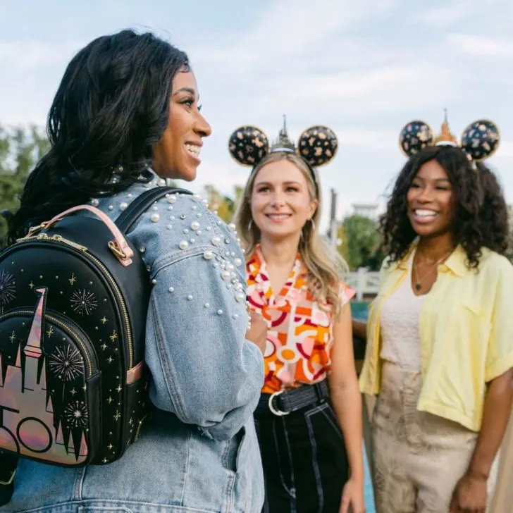 A group of 3 young women at Disney World wearing 50th Anniversary merchandise, such as Minnie Mouse ears and a backpack