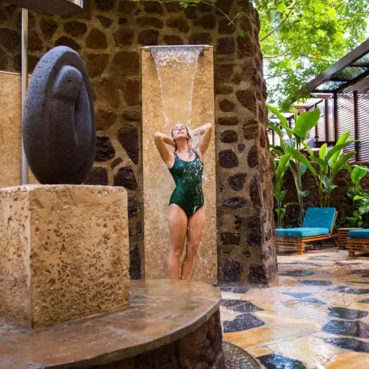 Photo of a woman in a swimsuit standing under a hydrotherapy shower at Laniwai Spa.