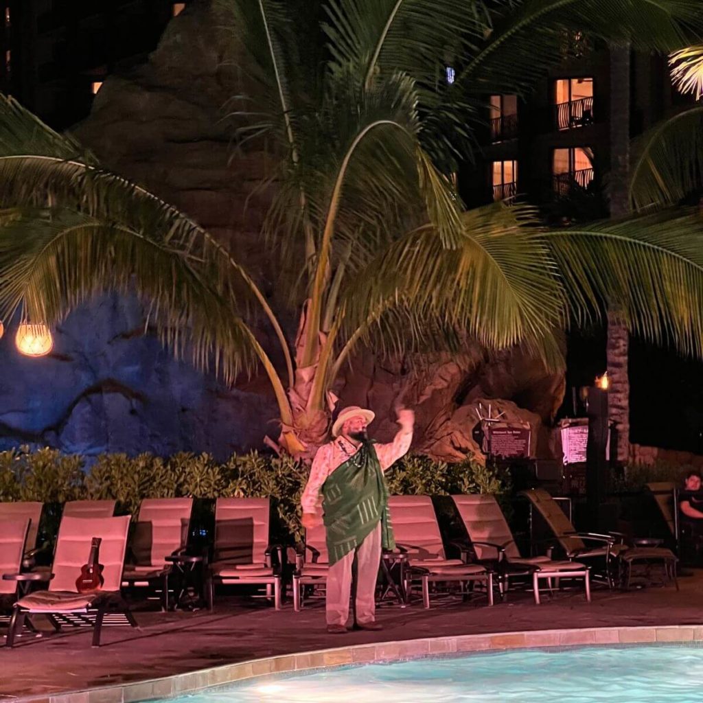Photo of a man telling Hawaiian folk tales at the Aulani pool area at night.