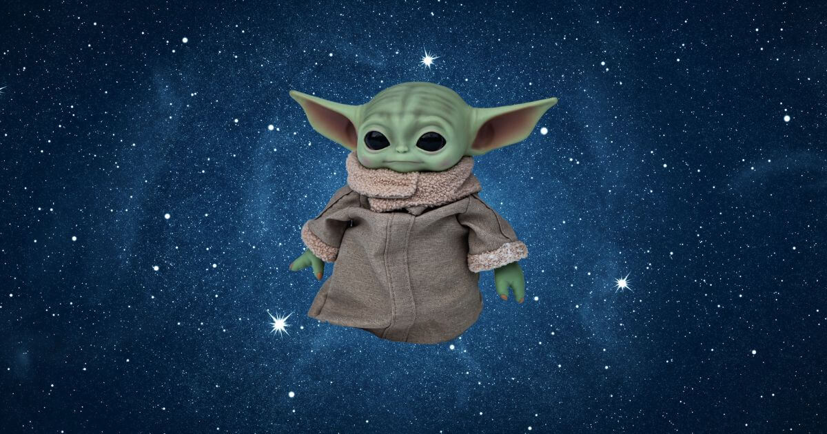 Photo of a Grogu toy floating against a blue starry sky background.