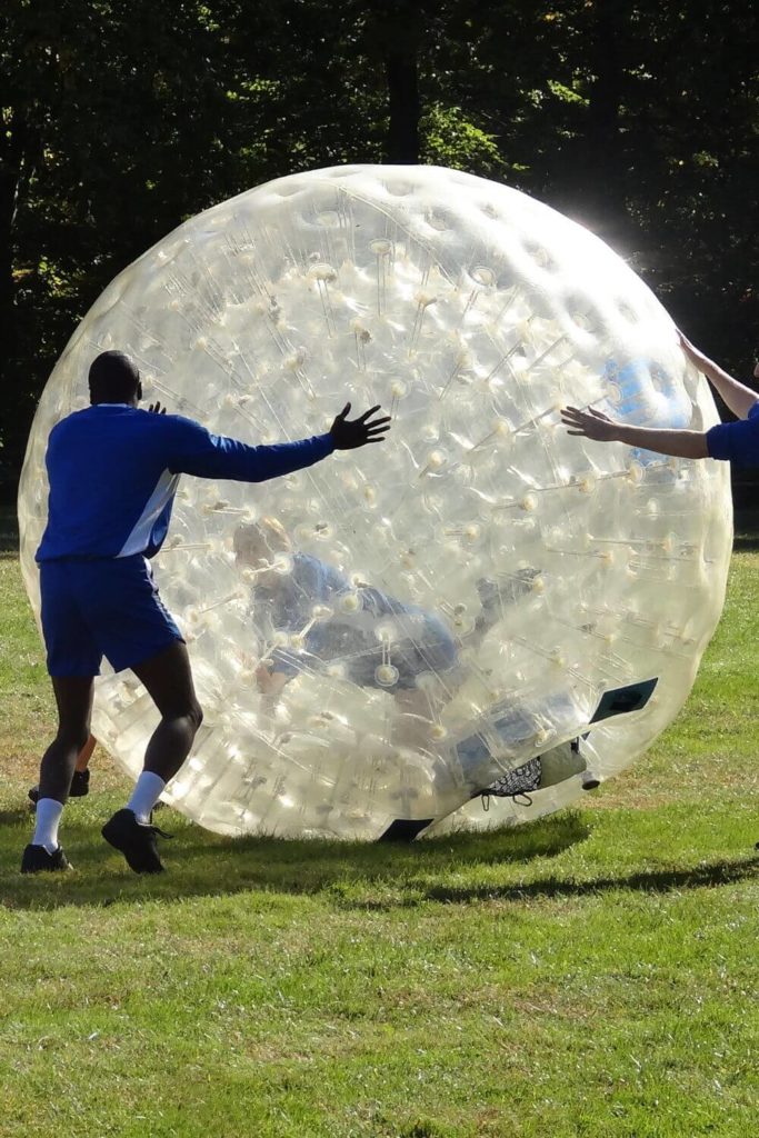 Photo of a group of adults playing a game with a giant inflatable hamster wheel like ball on the Nat Geo show, Brain Games.