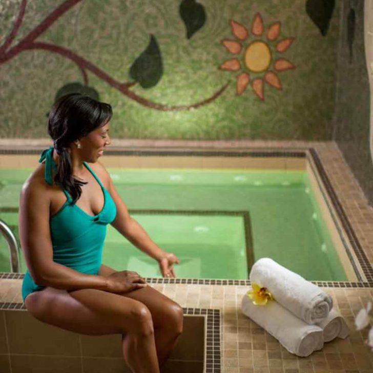 Photo of a woman sitting next to a whirlpool at a Disney World Spa, testing the temperature with her hand in the water.